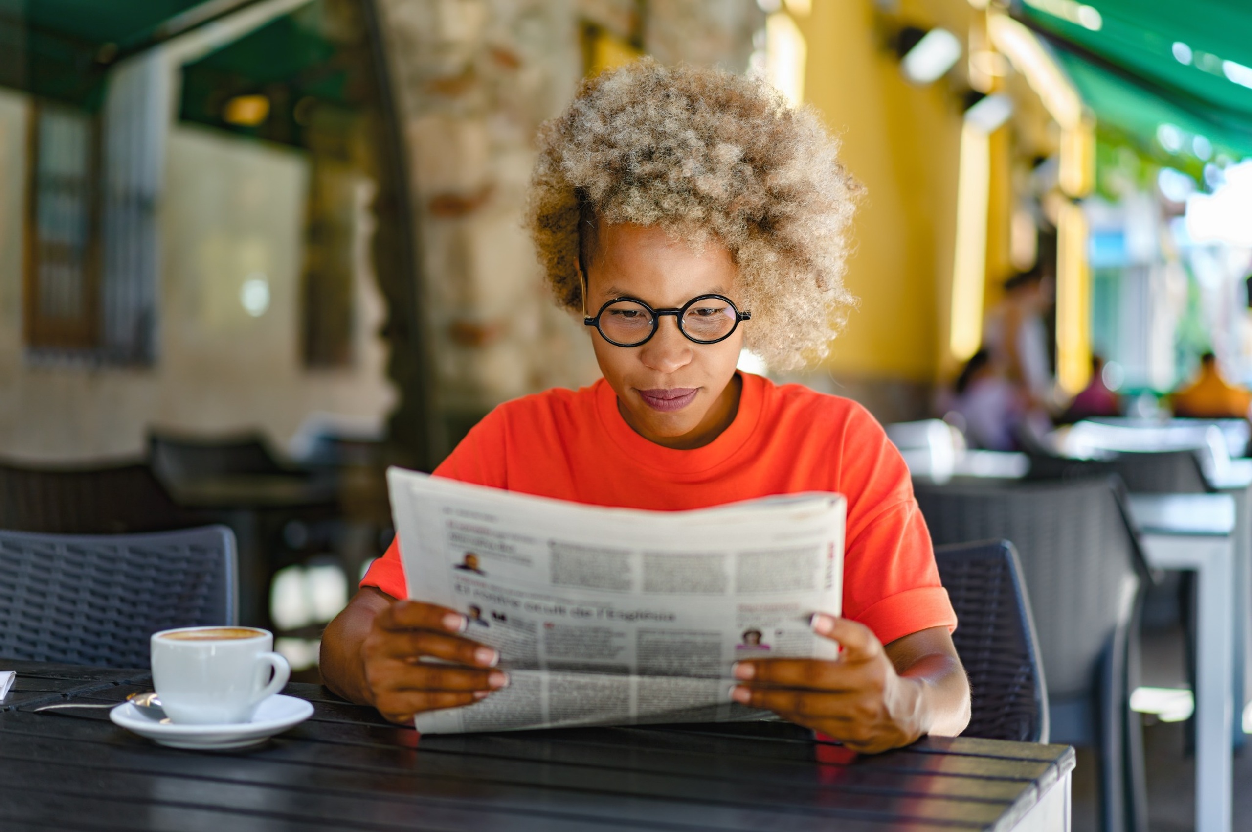 A woman reading a newspaper in a café.